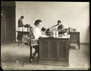 Indvendigt billede af en kvinde, der skriver fra en diktermaskine, og en mand, der dikterer ind i en anden på Edison Phonograph Co., West Orange, New Jersey, 1903 (sølv gelatinetryk)